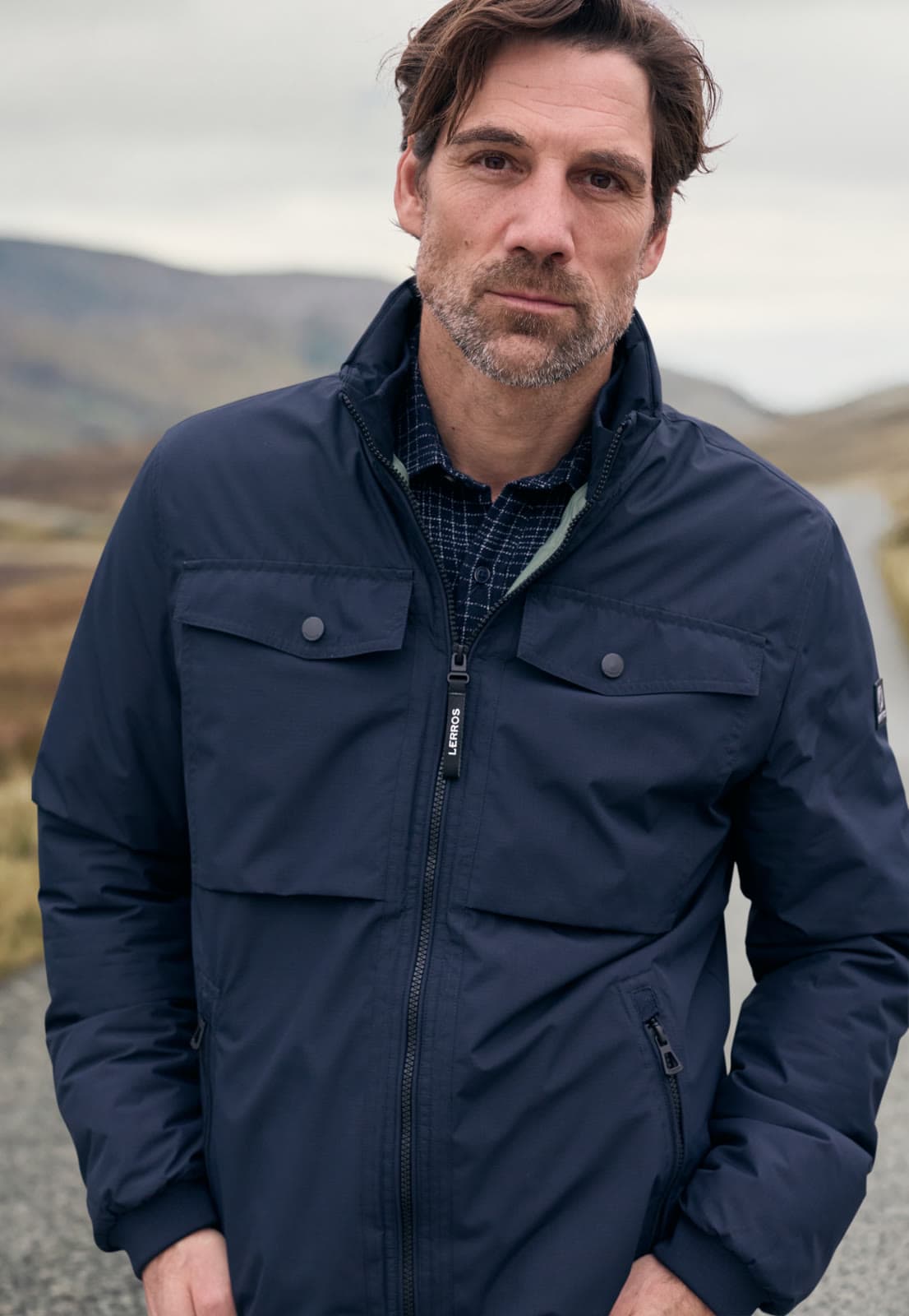 Man in een donkerblauw Lerros jack in een open landschap